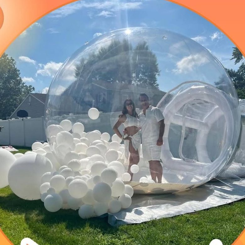 Couple dans la bulle transparente Bubbleland entourée de ballons blancs sur une pelouse